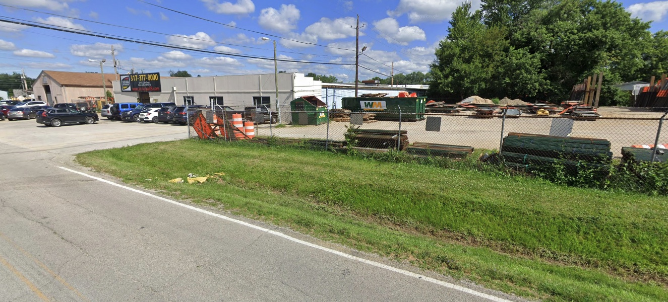 Street view of the buildings, parking lot and fenced yard along East 25th Street